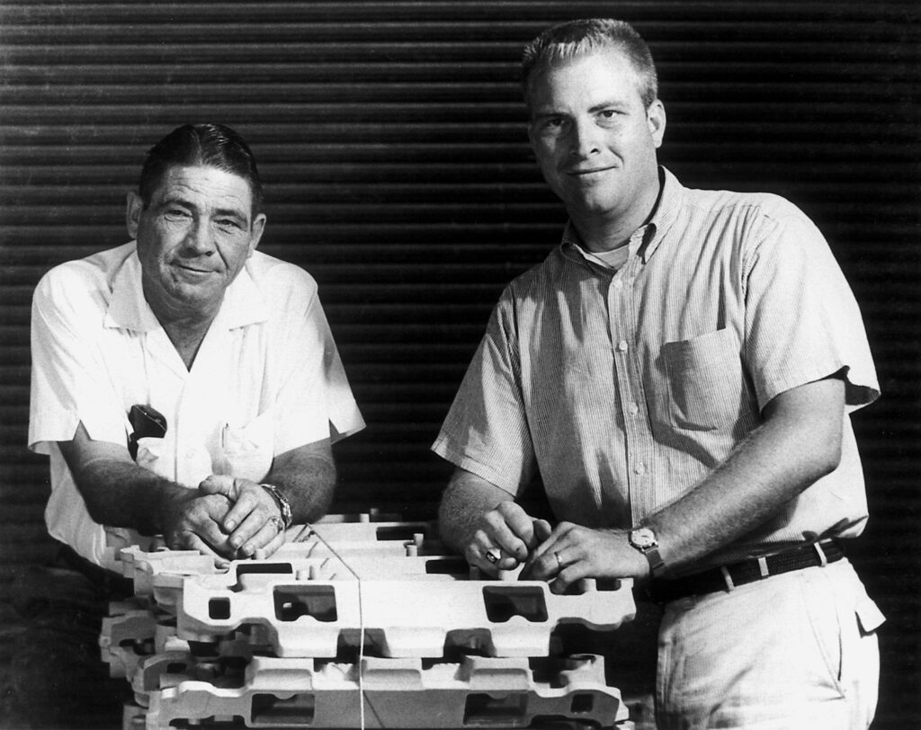 Vic Edlebrock Sr. and Vic Edelbrock Jr. posing on a stack of intake manifolds.