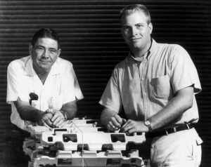 Vic Edlebrock Sr. and Vic Edelbrock Jr. posing on a stack of intake manifolds.
